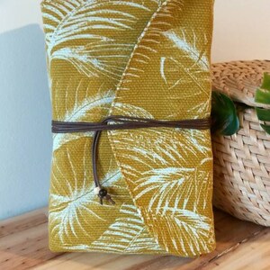 May include: A mustard yellow fabric pouch with a white tropical leaf pattern. The pouch has a brown leather strap and a white bead accent.