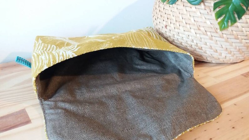 May include: A yellow fabric pouch with a white floral pattern. The pouch is open and the inside is lined with a brown fabric.