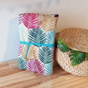 May include: A wrapped gift box with a tropical leaf pattern in shades of pink, green, and gold. The box is tied with a turquoise ribbon.