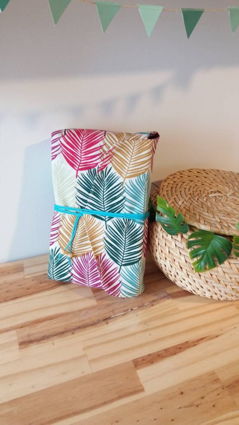 May include: A wrapped gift box with a tropical leaf pattern in shades of pink, green, and gold. The box is tied with a turquoise ribbon.