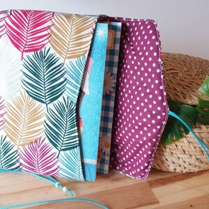 May include: A fabric envelope with a tropical leaf print on the outside and a pink polka dot print on the inside. The envelope is open and has a blue and white patterned fabric inside.
