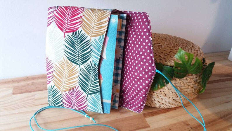 May include: A fabric envelope with a tropical leaf print on the outside and a pink polka dot print on the inside. The envelope is open and has a blue and white patterned fabric inside.