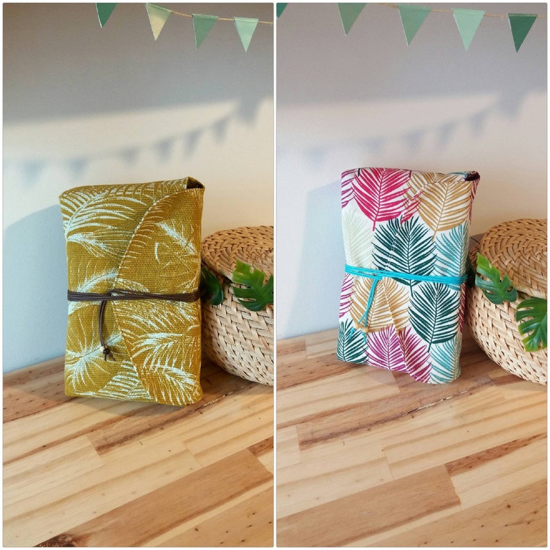 May include: Two fabric pouches with tropical leaf patterns. One pouch is mustard yellow with white leaves, the other is white with pink, green, and gold leaves. Both pouches have brown ties.