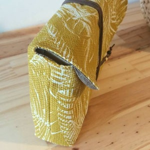 May include: A yellow fabric clutch with a white floral pattern. The clutch has a brown strap and a flap closure.