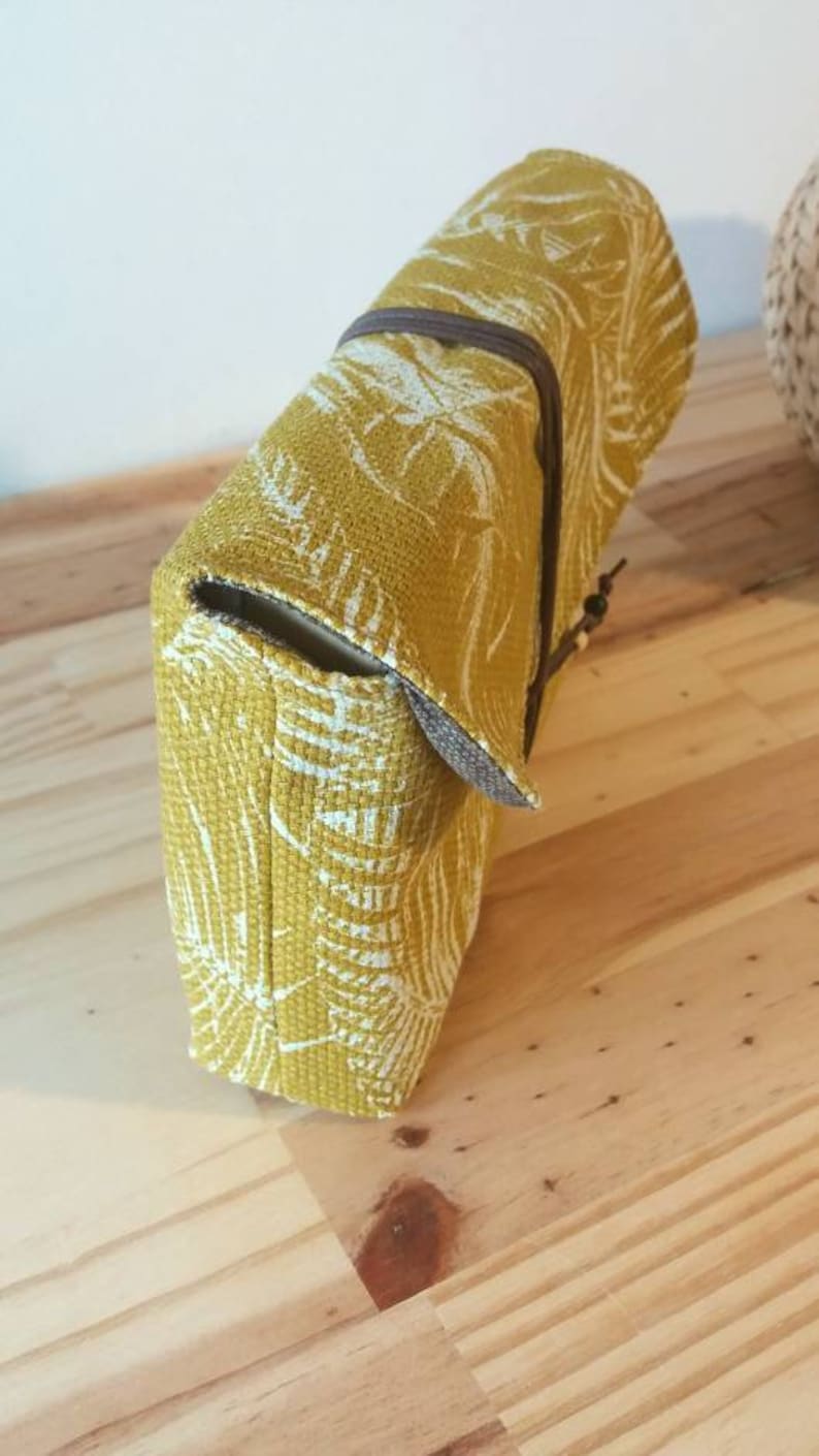 May include: A yellow fabric clutch with a white floral pattern. The clutch has a brown strap and a flap closure.