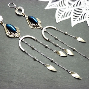 Peut inclure: Une paire de boucles d'oreilles pendantes argentées. Chaque boucle d'oreille présente une pierre ovale bleu foncé dans un cadre orné, avec une barre argentée incurvée et des chaînes pendantes avec des breloques en forme de feuille. Sur fond gris foncé.