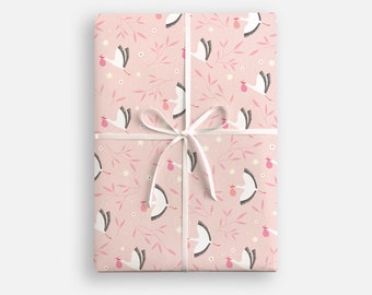 Peut inclure: Papier d'emballage rose avec un motif de cigognes blanches portant des paquets roses. Le papier est noué avec un ruban blanc.