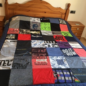 May include: A blue and grey patchwork quilt made from t-shirts. The quilt features various logos and designs, including "PINK FLOYD", "JUST DO IT", "BOSS", "DOCKAGE", and "DARK SIDE OF THE MOON".