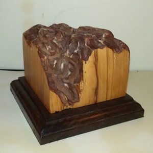 May include: A wooden sculpture of a mountain range, carved from a single piece of wood. The sculpture is mounted on a dark wood base.