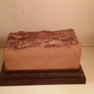 Peut inclure: Une boîte rectangulaire en bois avec un dessus brun et une base texturée de couleur brun clair. La boîte est en bois et a une finition naturelle.