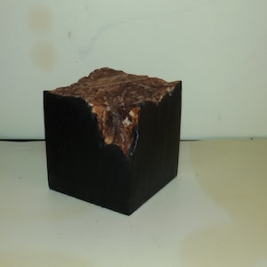 Könnte beinhalten: Ein kleiner, schwarzer Holzwürfel mit einer rauen, braunen, natürlichen Holzplatte.