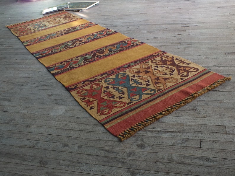 May include: A long, rectangular rug with a geometric pattern in shades of red, orange, yellow, blue, and brown. The rug has a fringe border.