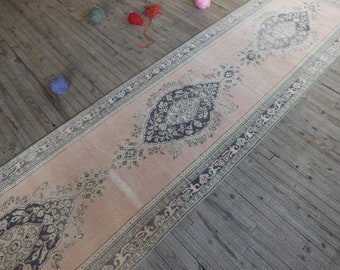 May include: A vintage pink and cream runner rug with a dark blue floral pattern. The rug has a fringed edge and is laid out on a wooden floor.