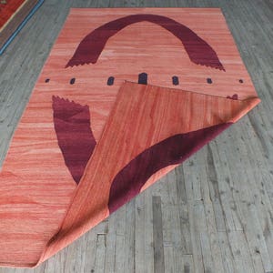 May include: A red and burgundy rug with a geometric design. The rug is folded in half and the design is visible on both sides.