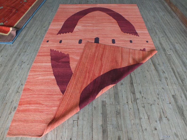 May include: A red and burgundy rug with a geometric design. The rug is folded in half and the design is visible on both sides.
