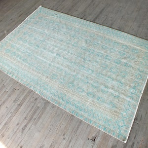 K&ouml;nnte beinhalten: Ein hellblauer und wei&szlig; gemusterter Teppich mit einem verblassten, Vintage-Look. Der Teppich hat einen Rand aus hellblauen und wei&szlig;en geometrischen Mustern.