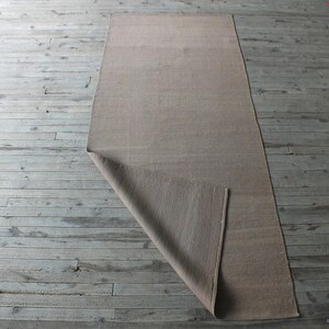 May include: A beige rug is folded in half and laid out on a wooden floor. The rug is made of a natural material and has a subtle texture.