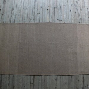 May include: A plain, light brown rug with a slightly textured surface. The rug is laid out on a wooden floor.