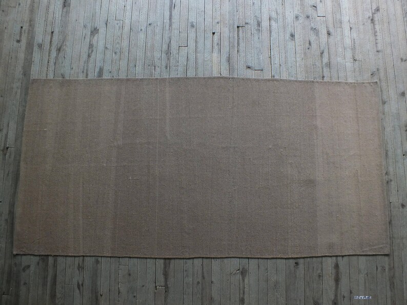 May include: A plain, light brown rug with a slightly textured surface. The rug is laid out on a wooden floor.
