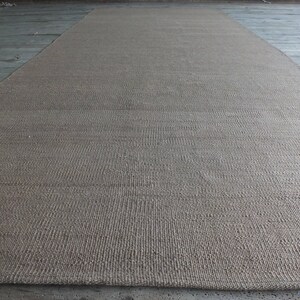 May include: A close-up of a natural fiber rug with a woven texture. The rug is a light brown color and has a subtle sheen.