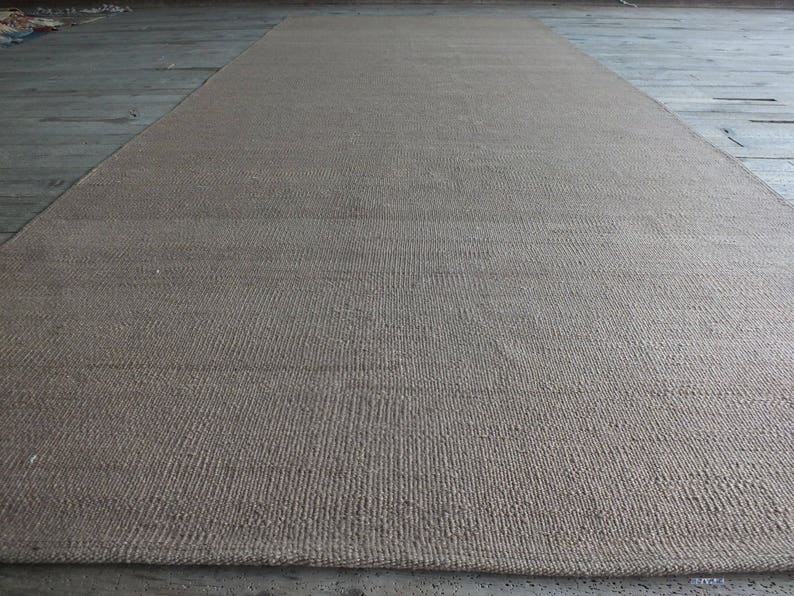 May include: A close-up of a natural fiber rug with a woven texture. The rug is a light brown color and has a subtle sheen.