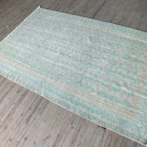 K&ouml;nnte beinhalten: Ein hellblauer und beiger Teppich mit geometrischem Muster. Der Teppich hat einen verblassten, Vintage-Look.