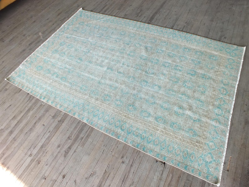 K&ouml;nnte beinhalten: Ein hellblauer und beiger Teppich mit geometrischem Muster. Der Teppich hat einen verblassten, Vintage-Look.