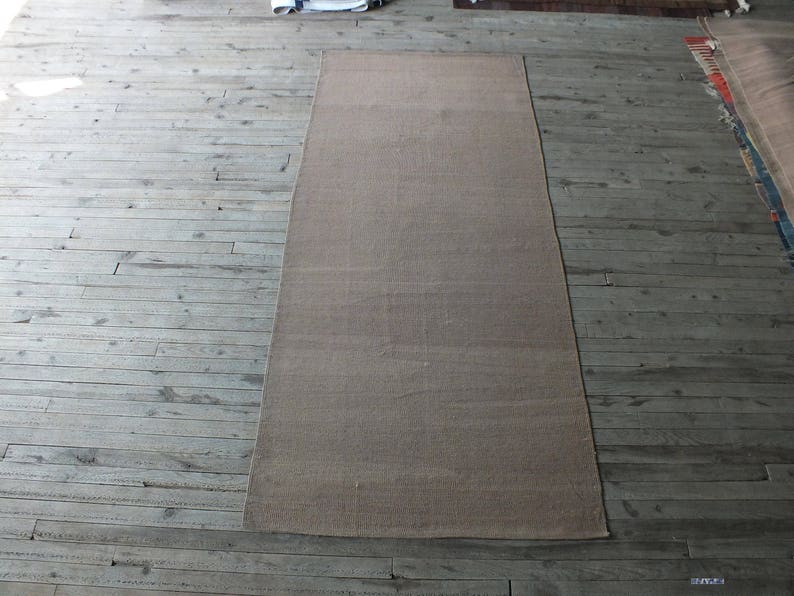 May include: A light brown rectangular rug with a subtle woven texture. The rug is laid out on a wooden floor.