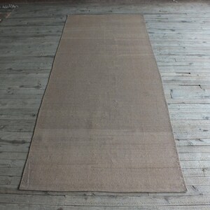 May include: A light brown rectangular rug with a subtle woven texture. The rug is laid out on a wooden floor.