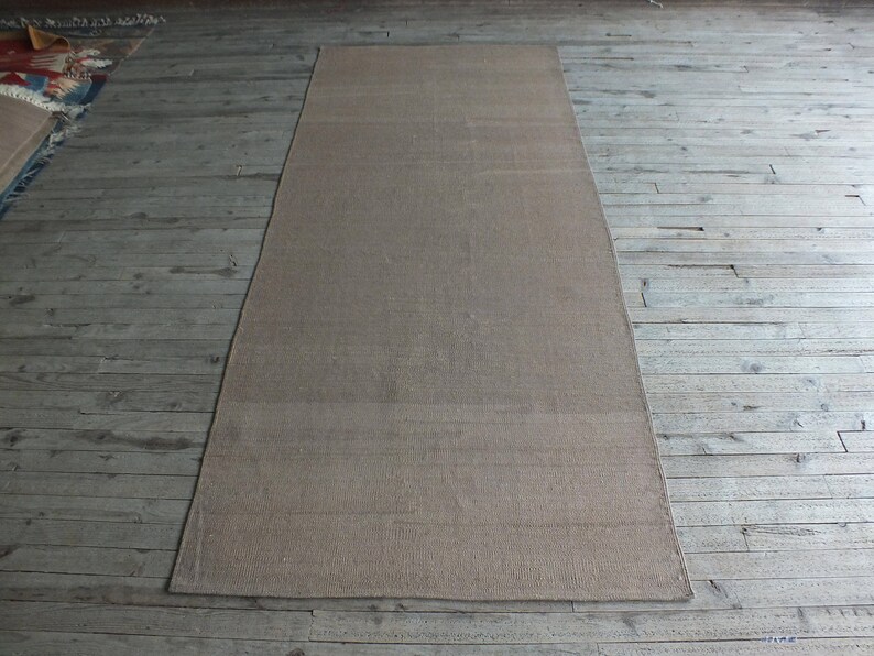 May include: A light brown rectangular rug with a subtle woven texture. The rug is laid out on a wooden floor.