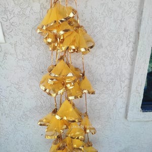 May include: A string of yellow fabric tassels with gold trim hanging from a ceiling. The tassels are made of sheer fabric and have a delicate, flowing appearance.