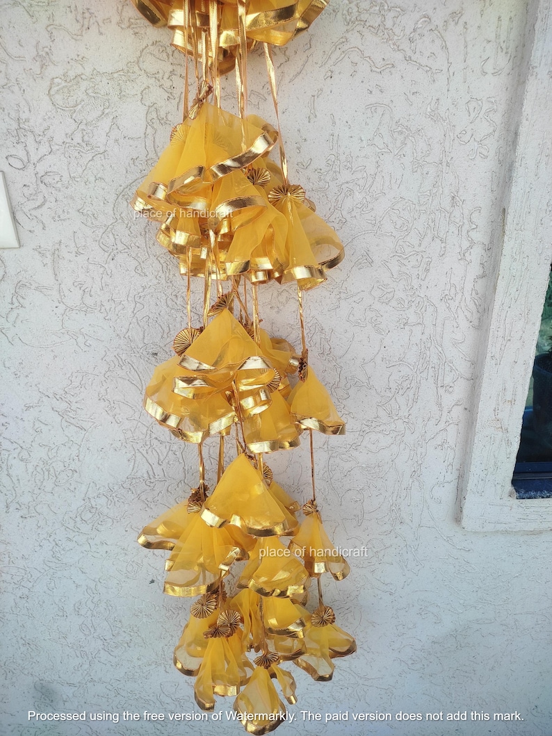 May include: A string of yellow fabric tassels with gold trim hanging from a ceiling. The tassels are made of sheer fabric and have a delicate, flowing appearance.