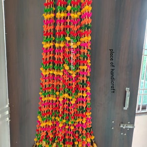 May include: A colorful door hanging with pom-poms and bells. The hanging is made of green, pink, yellow, orange, and red pom-poms. The hanging is decorated with gold bells. The hanging is attached to a door with a silver hook. The text "place of handicraft" is visible in the image.