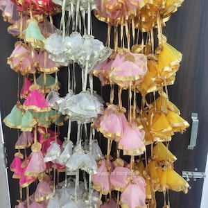 May include: A collection of decorative hanging pouches made of sheer fabric with gold trim. The pouches are in various colors, including pink, yellow, green, and white.