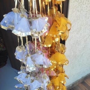 May include: A collection of decorative hanging pouches made of sheer fabric in white, yellow, and pink. The pouches have gold trim and are strung together with gold ribbon.