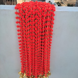 May include: A long garland of red pom-poms with gold bells at the bottom.