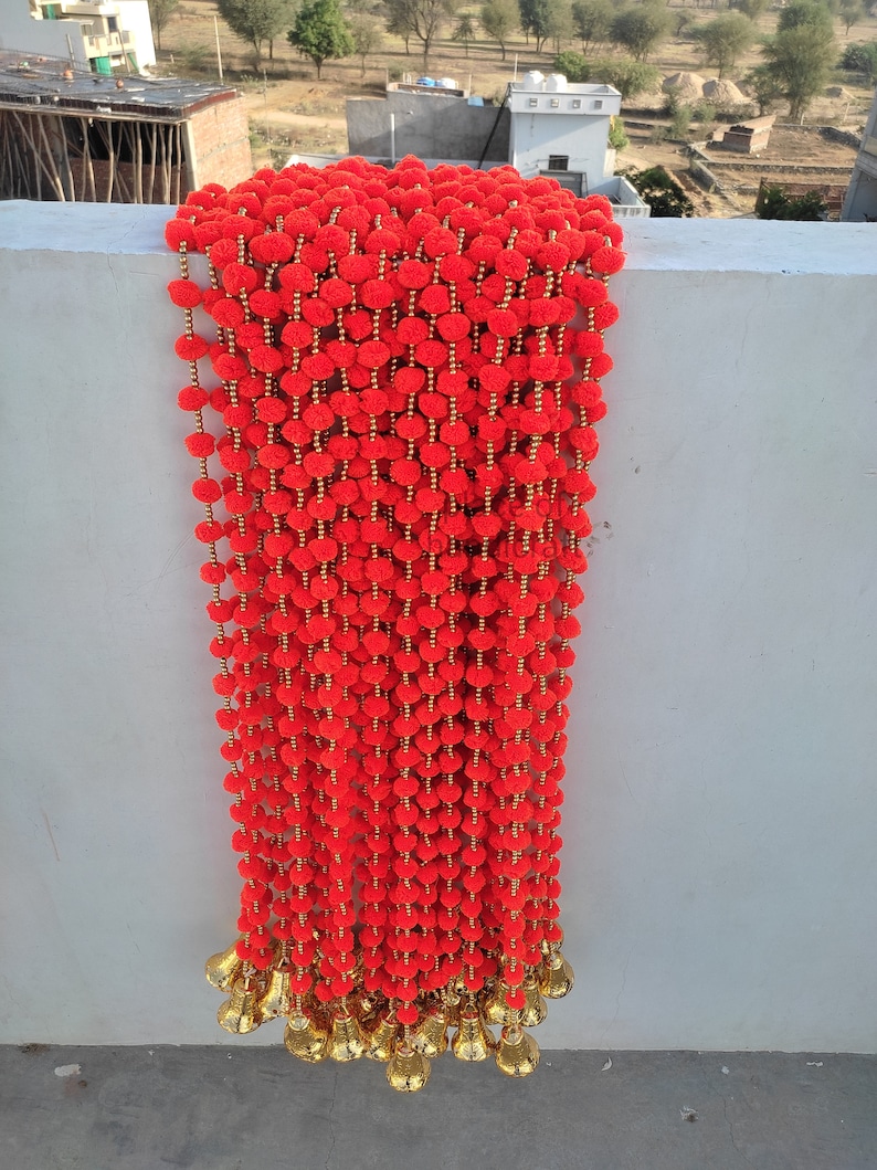 May include: A long garland of red pom-poms with gold bells at the bottom.