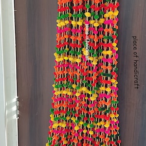 May include: Multicoloured pom-pom garland with gold bells. The garland is made of small, fluffy balls in shades of pink, orange, yellow, and green. The garland is strung together with gold beads and has a row of gold bells at the bottom.