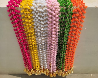 May include: A set of colorful pom-pom garlands with gold bells at the bottom. The garlands are in pink, yellow, white, green, and orange.