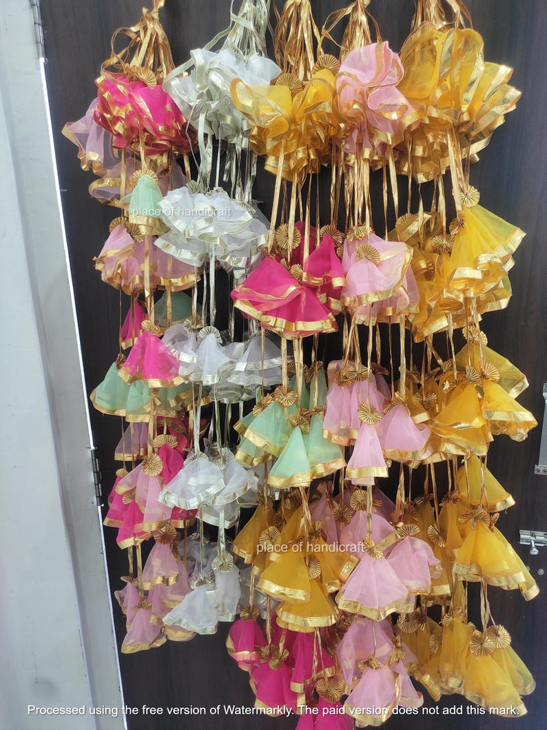 May include: A collection of colorful fabric pouches with gold trim and tassels hanging from a string. The pouches are made of sheer fabric and are arranged in a variety of colors, including pink, yellow, green, and white.