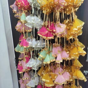 May include: A collection of colorful fabric pouches with gold trim and tassels hanging from a string. The pouches are made of sheer fabric and are arranged in a variety of colors, including pink, yellow, green, and white.