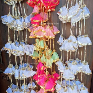 May include: A string of decorative hanging ornaments made of sheer fabric with gold trim. The ornaments are in shades of white, pink, green, and red.