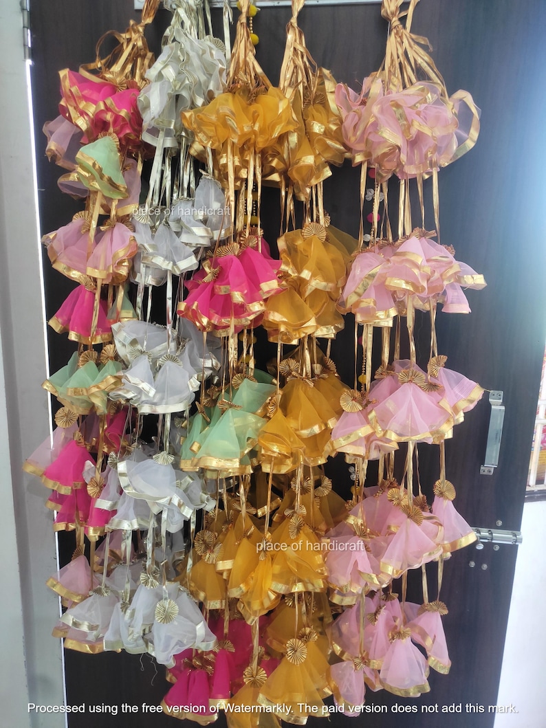 May include: A display of colorful fabric garlands with gold trim. The garlands are made of multiple layers of sheer fabric and are tied together with gold ribbon. The garlands are hanging from a door frame.
