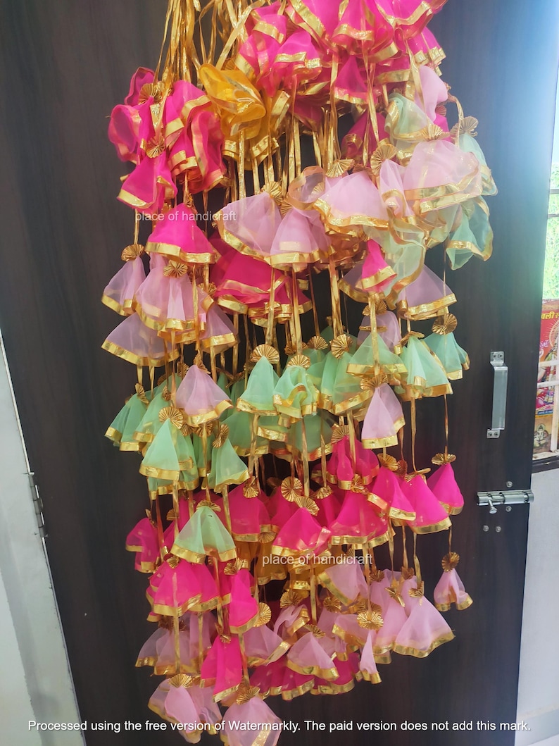 May include: A collection of colorful fabric pouches with gold trim and ribbons hanging from a door. The pouches are made of pink, green, and yellow fabric and are decorated with gold trim and ribbons.