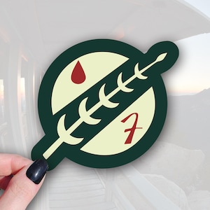 May include: A green and white sticker with a red drop of blood and a stylized plant with a red "F" in the center. The sticker is a parody of the Mandalorian symbol.