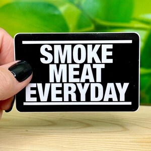 May include: Black and white sticker with the text "SMOKE MEAT EVERYDAY" in white letters on a black background.