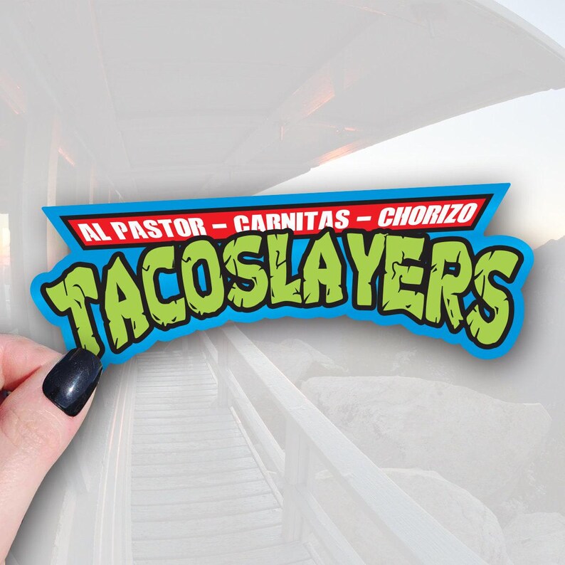 A sticker with the text TACOS LAYERS in a stylized font, with the words AL PASTER - CARNITAS - CHORIZO written above it.