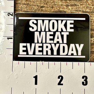 May include: Black and white sticker with the text "SMOKE MEAT EVERYDAY" printed in white on a black background.