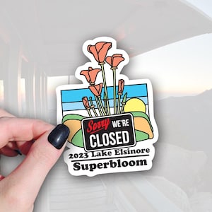 May include: A sticker featuring a stylized illustration of California poppies with the text "Sorry We're Closed" and "2023 Lake Elsinore Superbloom." The design includes a landscape with a blue sky, green hills, and a yellow sun.