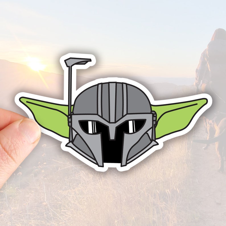 May include: A green and gray sticker of a cartoon character wearing a helmet with a visor. The character has large ears and a small mouth.